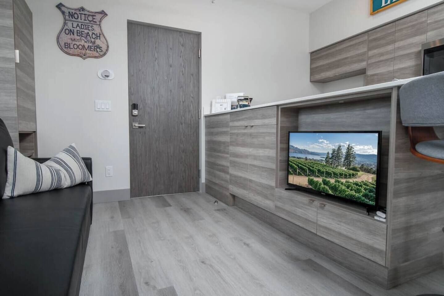 A modern living room with a TV mounted on a wooden wall, a dark-colored sofa, and a door with a vintage sign.