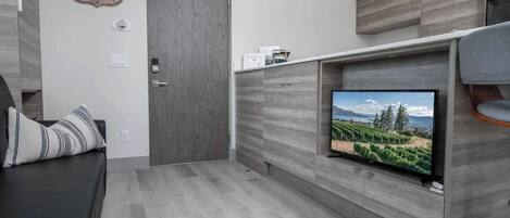 A modern living room with a TV mounted on a wooden wall, a dark-colored sofa, and a door with a vintage sign.