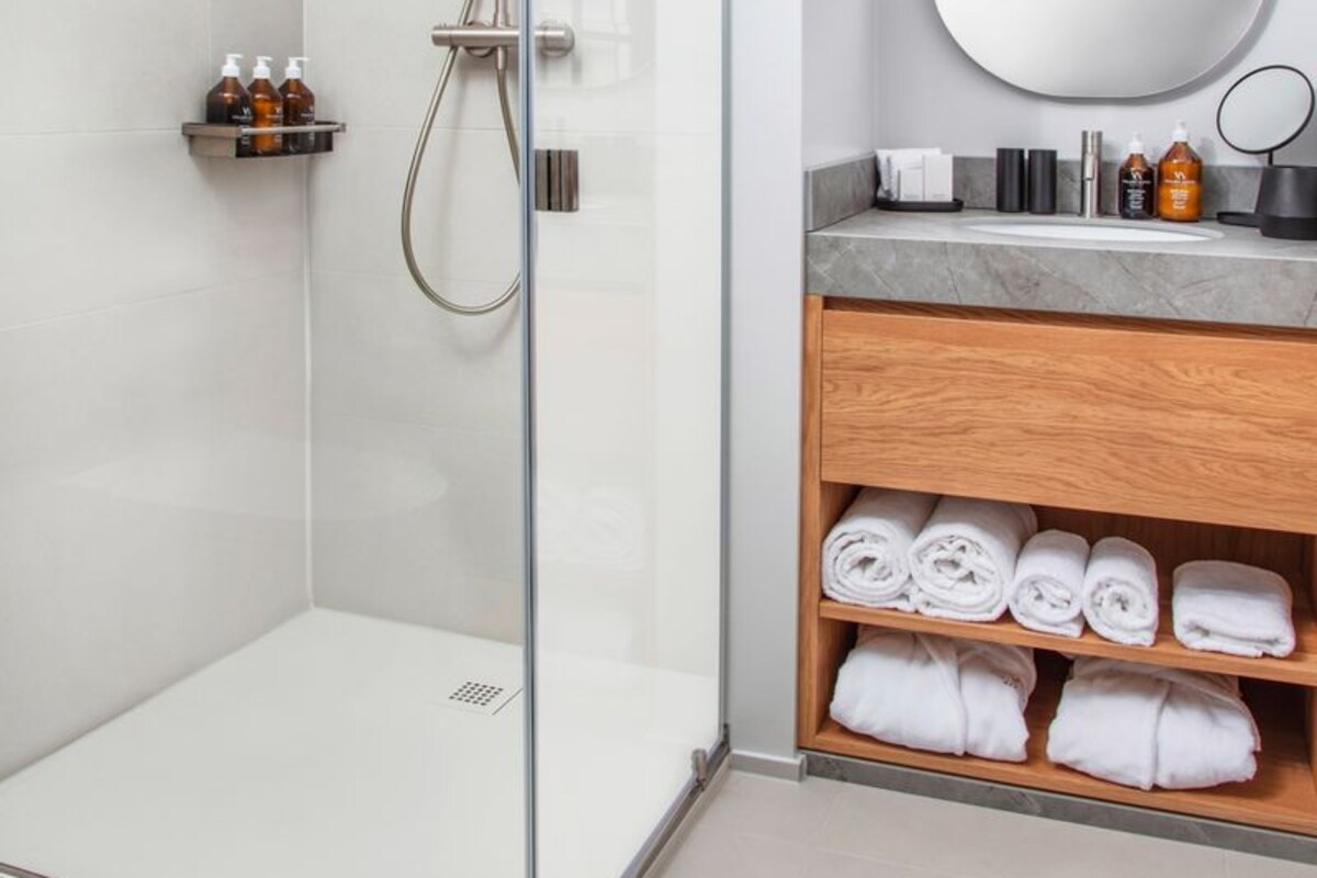 A modern bathroom with a glass-enclosed shower, a wooden vanity with a mirror, and neatly folded towels.