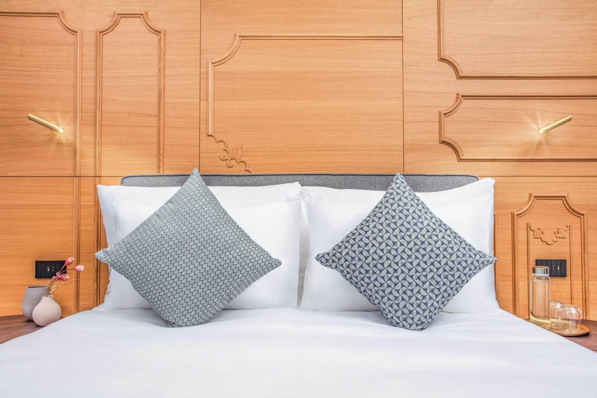 Ein Bett mit zwei gemusterten Kissen, einem Holzkopfstück und einem Nachttisch mit einer Vase und Gläsern.