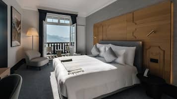 A hotel room with a large bed, a wooden headboard, a balcony with a view of mountains, a chair, and a lamp.