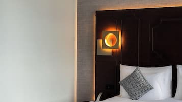 Une chambre d’hôtel au design moderne, dotée d’un grand lit avec du linge de lit blanc, d’une tête de lit sombre et d’un luminaire mural original.