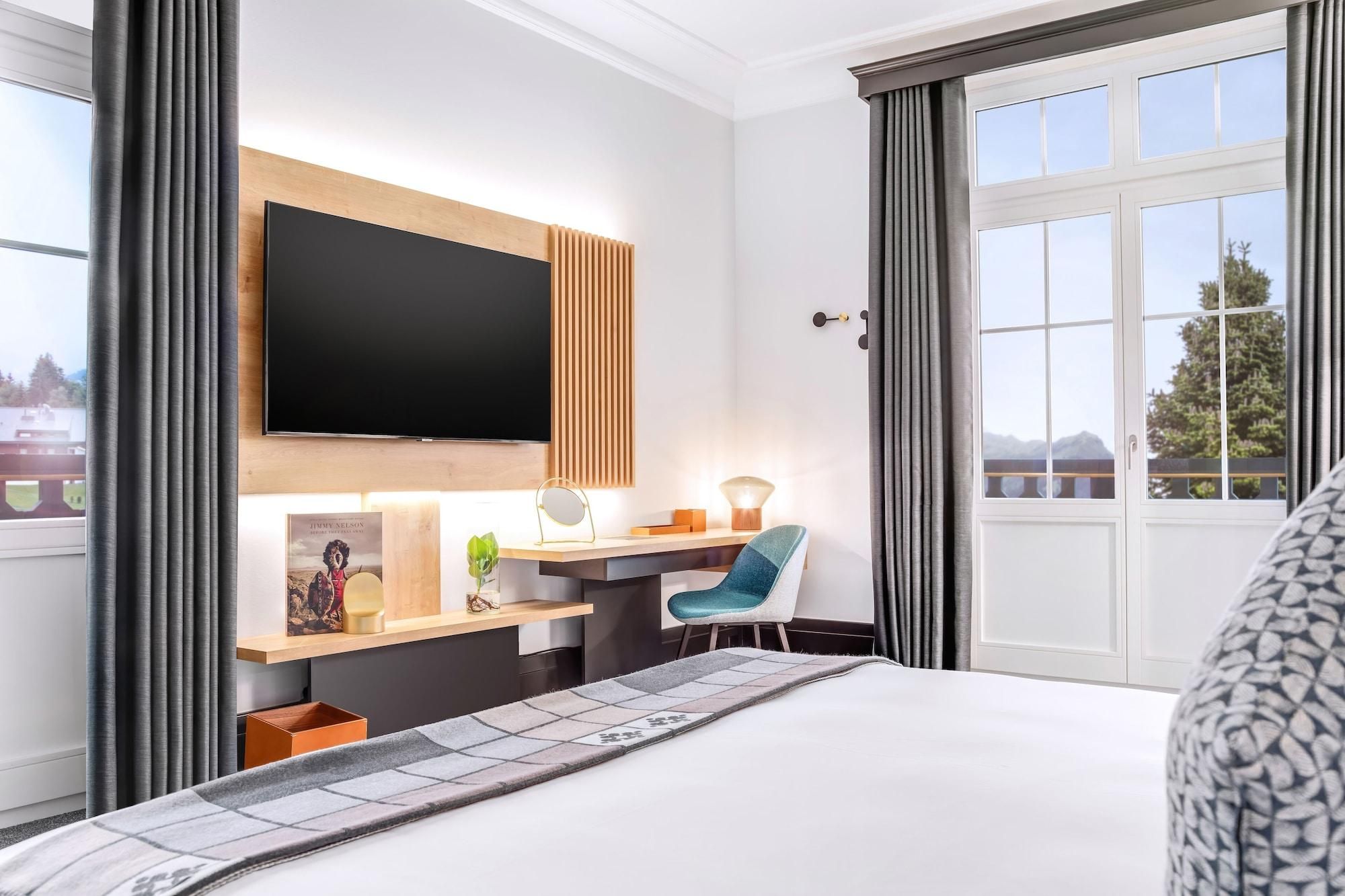 A hotel room with a bed, a desk with a chair, a TV, and a window with a view of the outdoors.