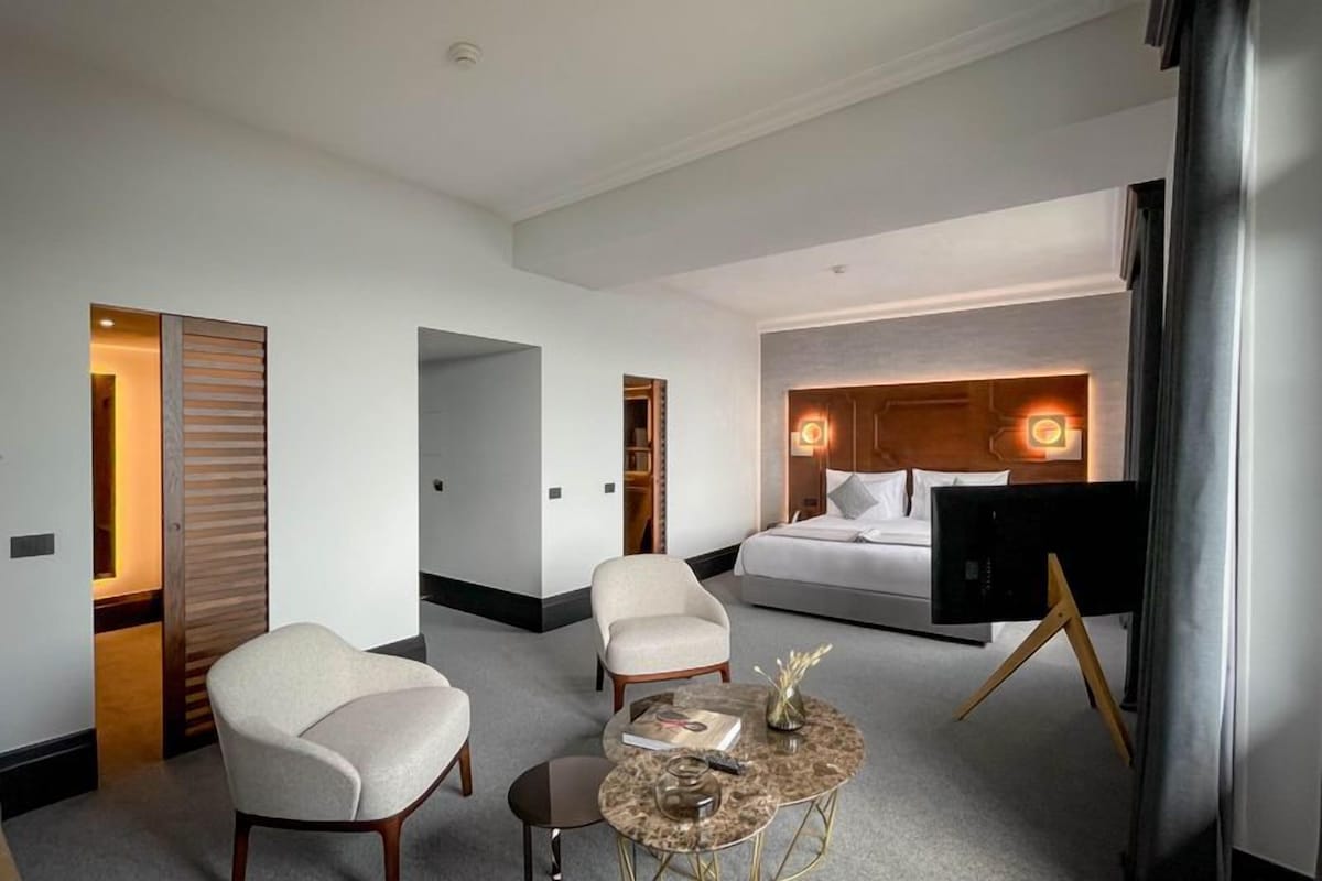 A hotel room with a bed, two armchairs, a small coffee table, and a TV.