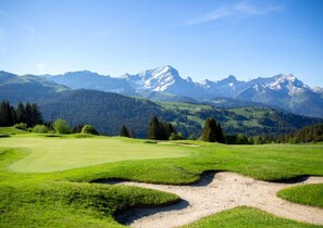 Ein Golfplatz mit freiem Blick auf schneebedeckte Berge im Hintergrund.