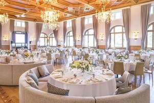 Una sala banchetti con tavoli rotondi apparecchiati per la cena, ampie finestre e lampadari.