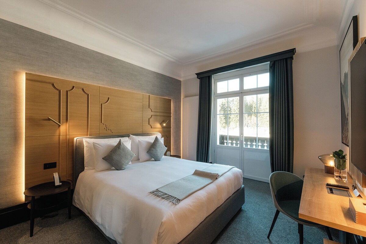 A hotel room with a large bed, a desk, and a window with curtains.