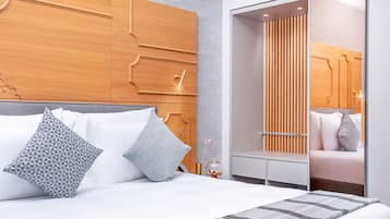 Une chambre d’hôtel moderne avec un grand lit, une tête de lit en bois, une armoire avec un miroir et une table de chevet avec une lampe.