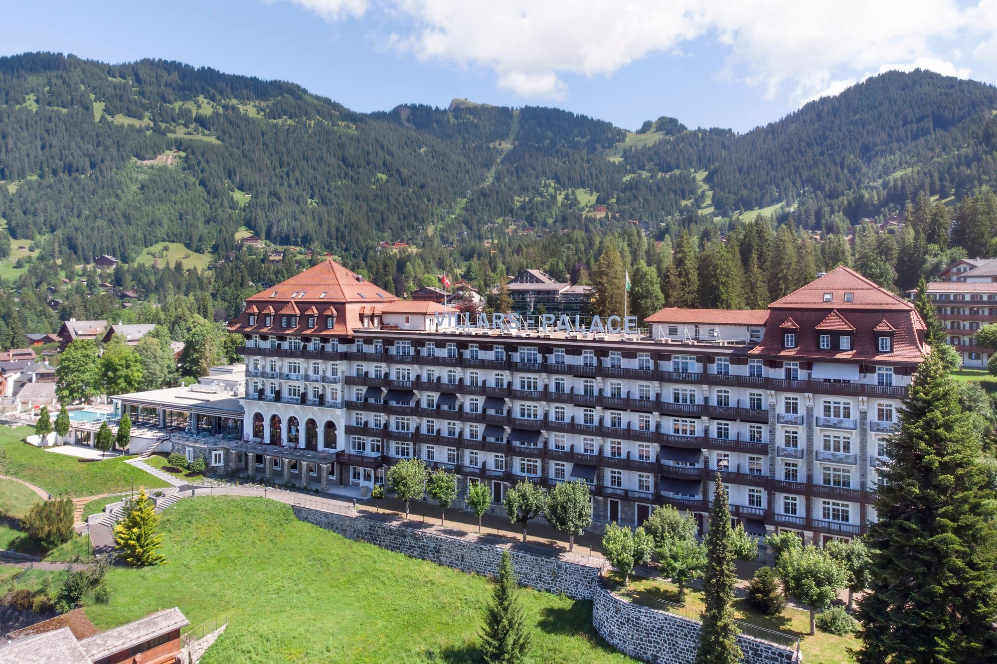 A large hotel with multiple floors and a red roof, surrounded by lush greenery and mountains.