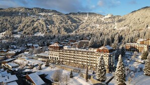 Ein großes Hotel mit mehreren Etagen und einem zentralen Innenhof, umgeben von schneebedeckten Bäumen und Bergen.
