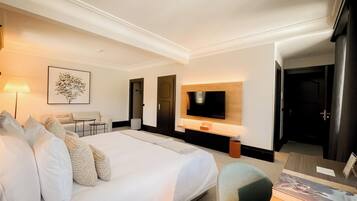 A hotel room with a large bed, a desk, a chair, a TV mounted on the wall, and a framed picture on the wall.