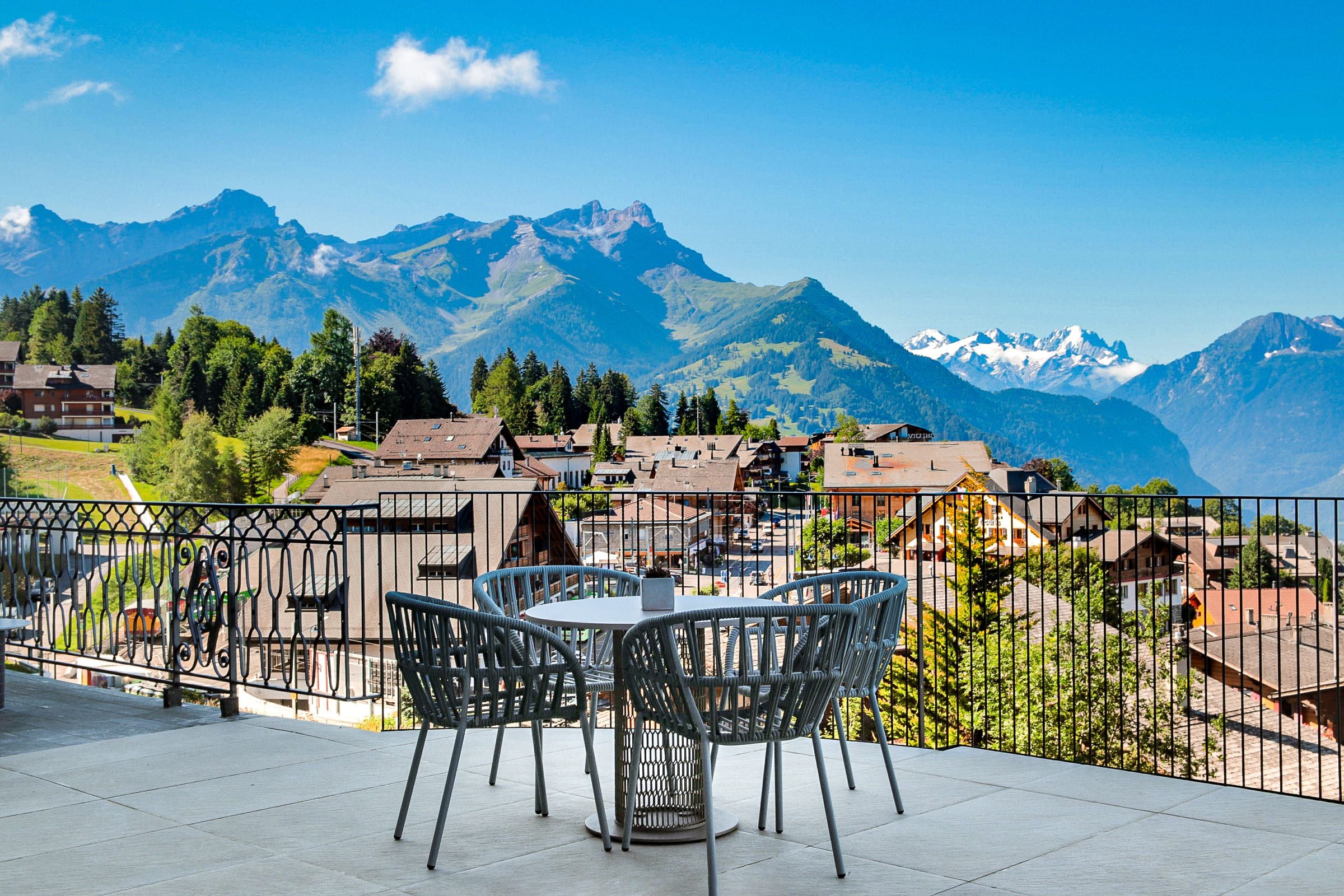 A terrace with a table and chairs overlooking a mountainous landscape with houses and trees.