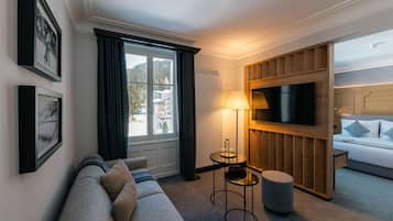 Ein modernes Hotelzimmer mit Sofa, einem an einer Holzvertäfelung montierten Fernseher, einer Lampe und Blick ins Freie.