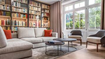 Ein Wohnzimmer mit einem Ecksofa, zwei Sesseln, einem Couchtisch und einem großen Bücherregal voller Bücher.