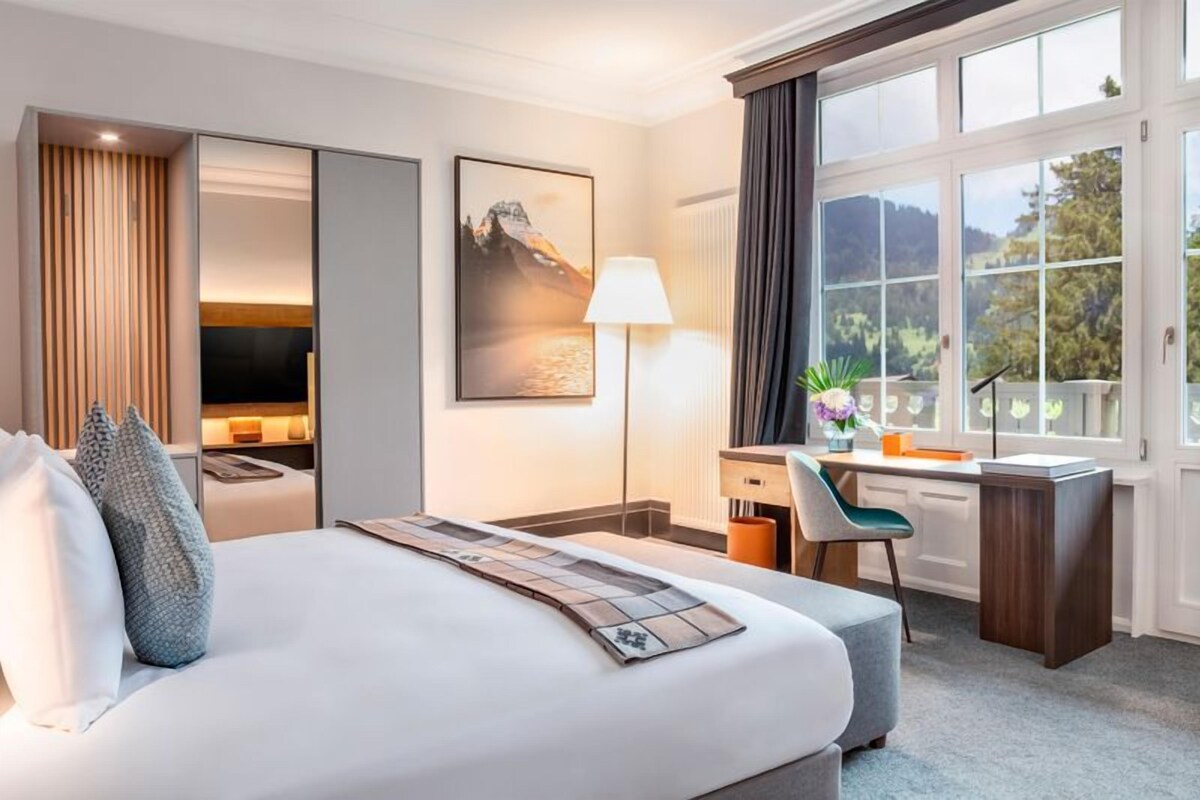 A hotel room with a bed, desk, chair, and large windows.
