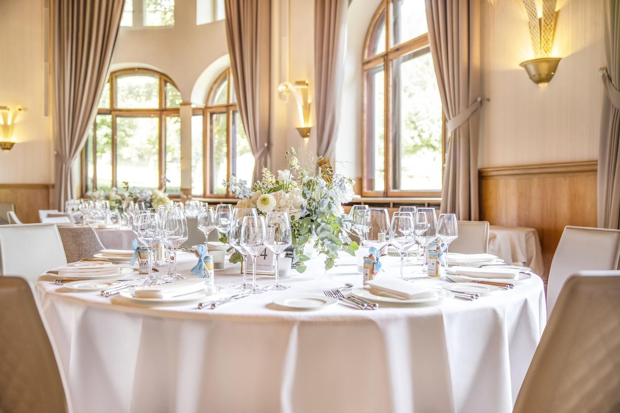 A banquet hall with round tables set for a formal event, featuring white tablecloths, glassware, and floral centerpieces.