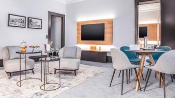 A modern hotel room with a sofa, two armchairs, a coffee table, a TV mounted on the wall, and a large mirror.