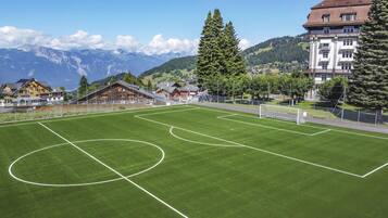 Un terrain de football avec des poteaux de but, entouré de bâtiments et avec des montagnes en arrière-plan.