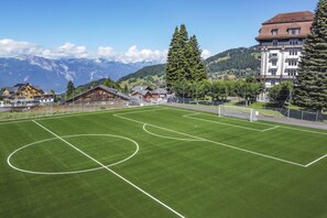 A soccer field with goalposts, surrounded by buildings and mountains in the background. - Villars Palace (Ollon)