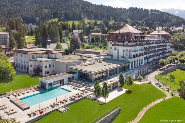 A resort with a swimming pool, outdoor seating, and a large building with multiple balconies. - Villars Palace (Ollon)