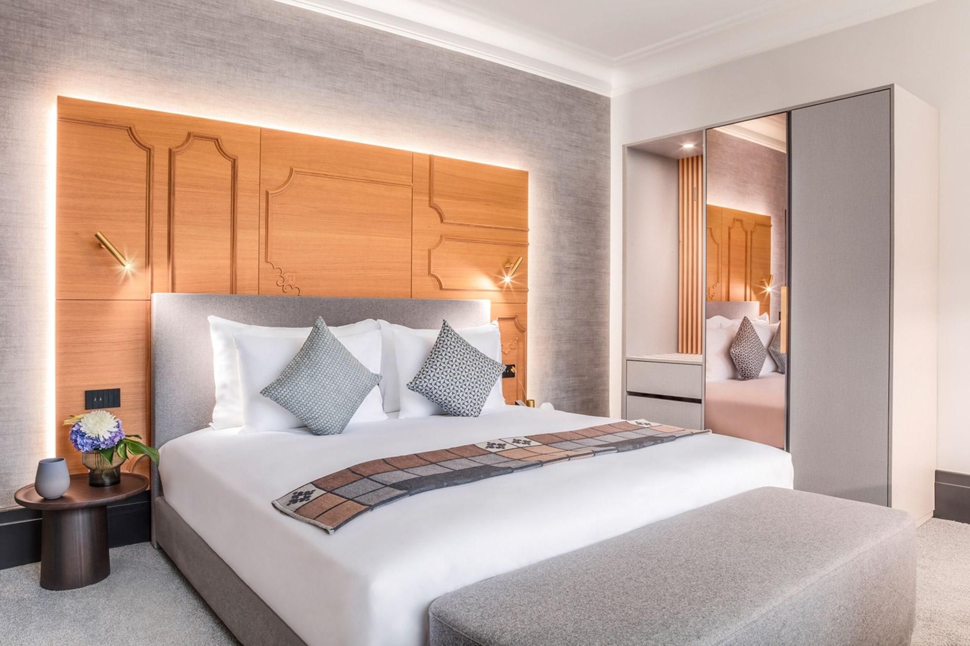 Ein modernes Hotelzimmer mit einem großen Bett, einem hölzernen Kopfteil, einem Nachttisch mit einer Vase und einem Spiegel.