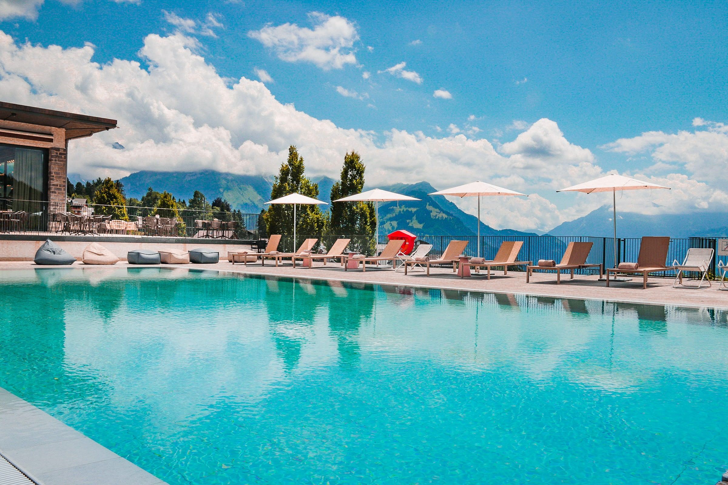 Un espace piscine agrémenté de chaises longues et de parasols, le tout entouré de montagnes.