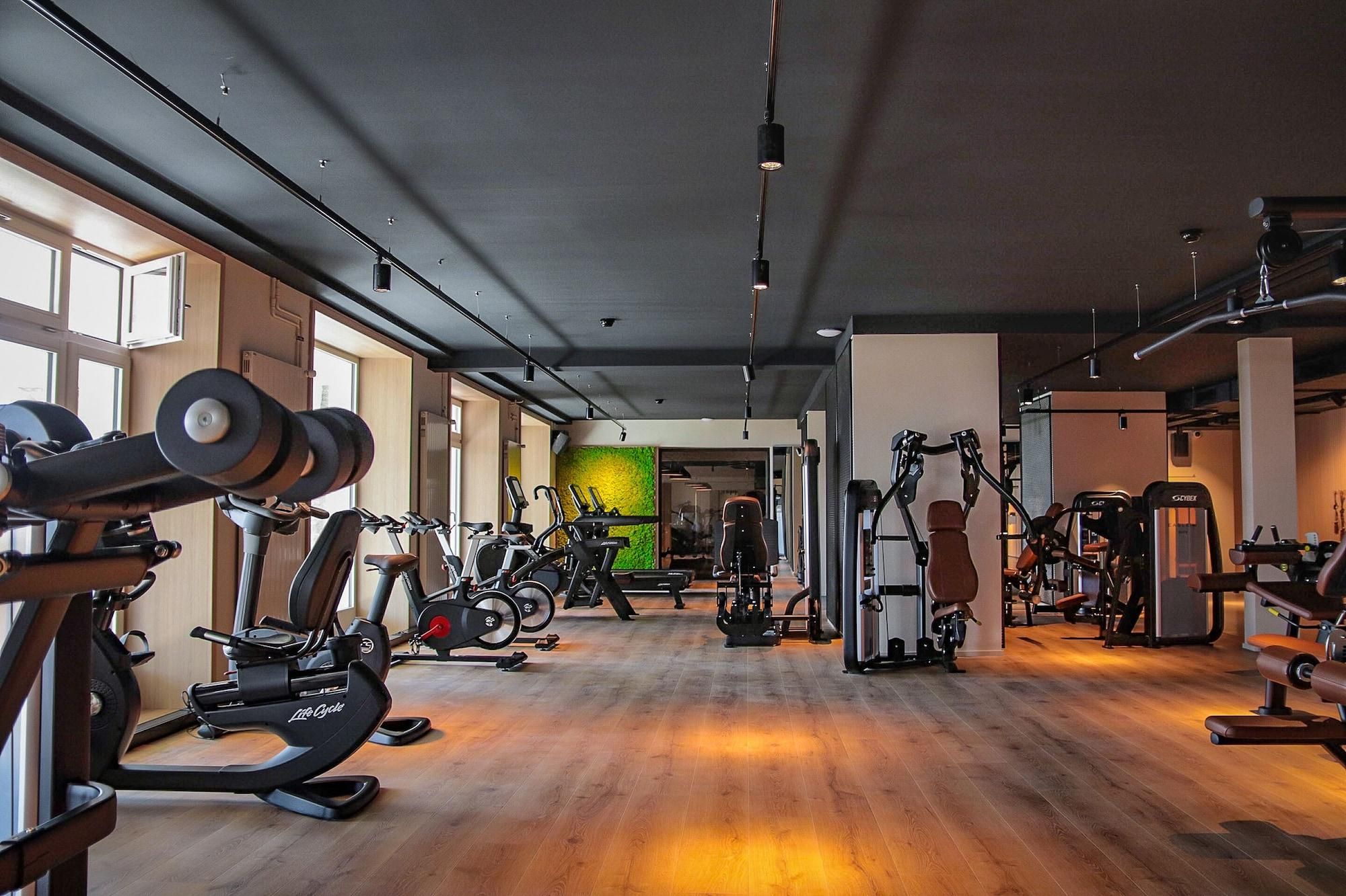 Een fitnessruimte met cardioapparatuur, krachttrainingapparatuur en een groene wand.