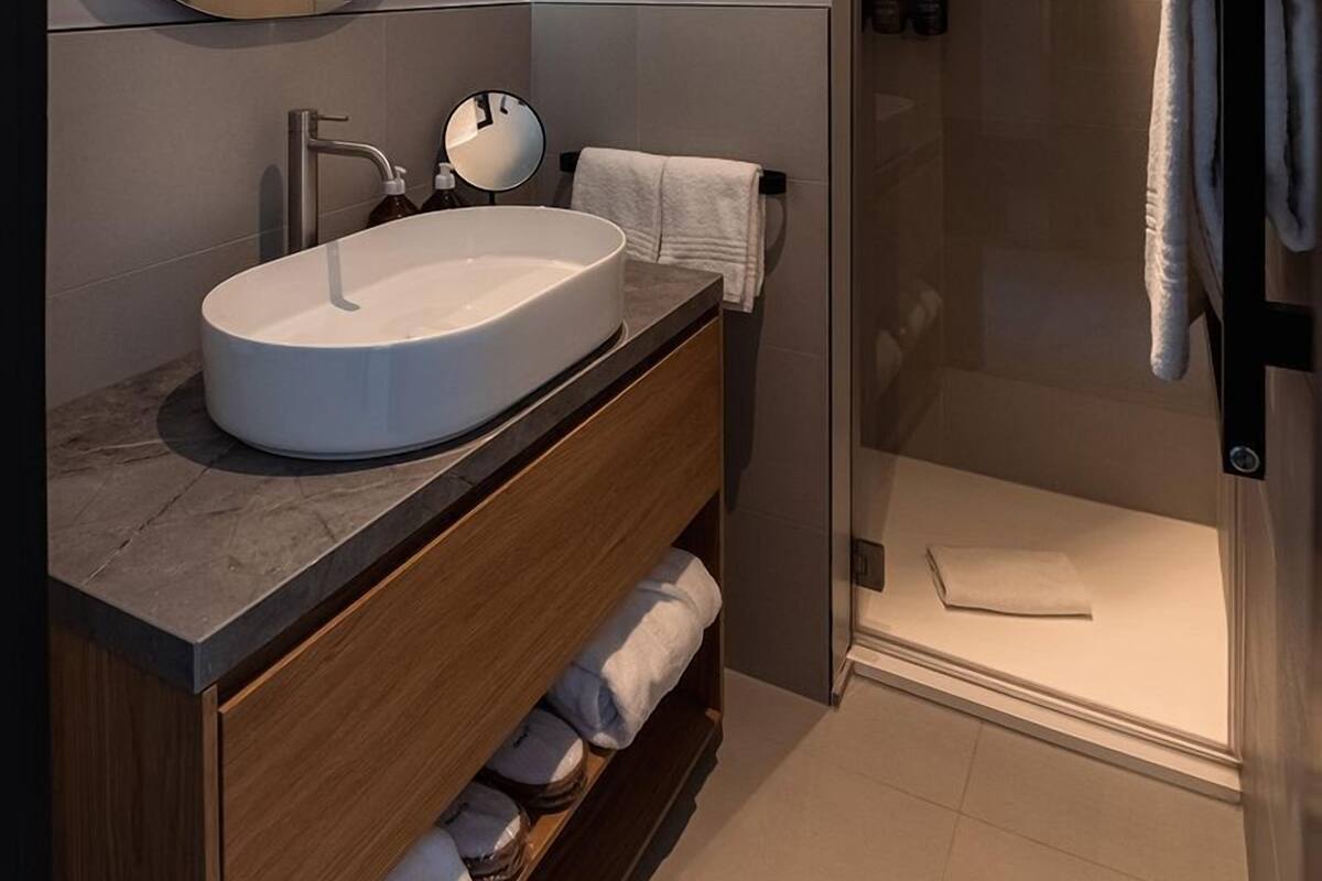 A modern bathroom with a large oval sink, a round mirror, and a glass-enclosed shower area.