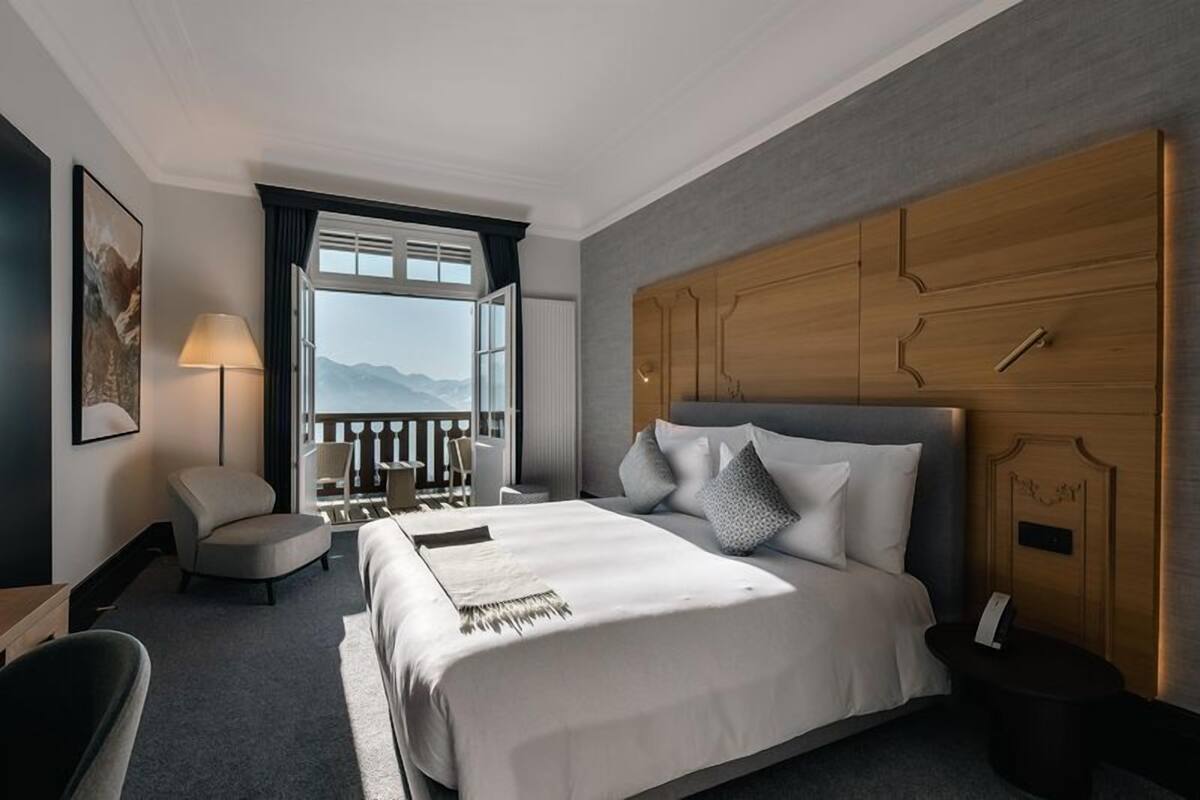 A hotel room with a large bed, a wooden headboard, a balcony with a view, a chair, and a lamp.