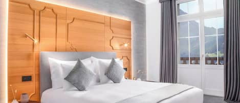 A modern hotel room with a large bed, a wooden headboard, and a view of mountains through the window.