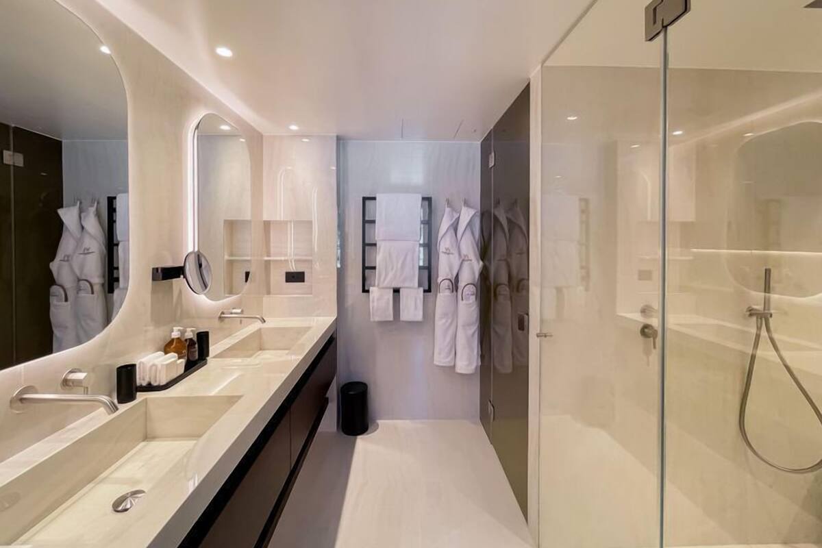 A modern bathroom with a large mirror, dual sinks, a glass shower enclosure, and a towel rack with robes.