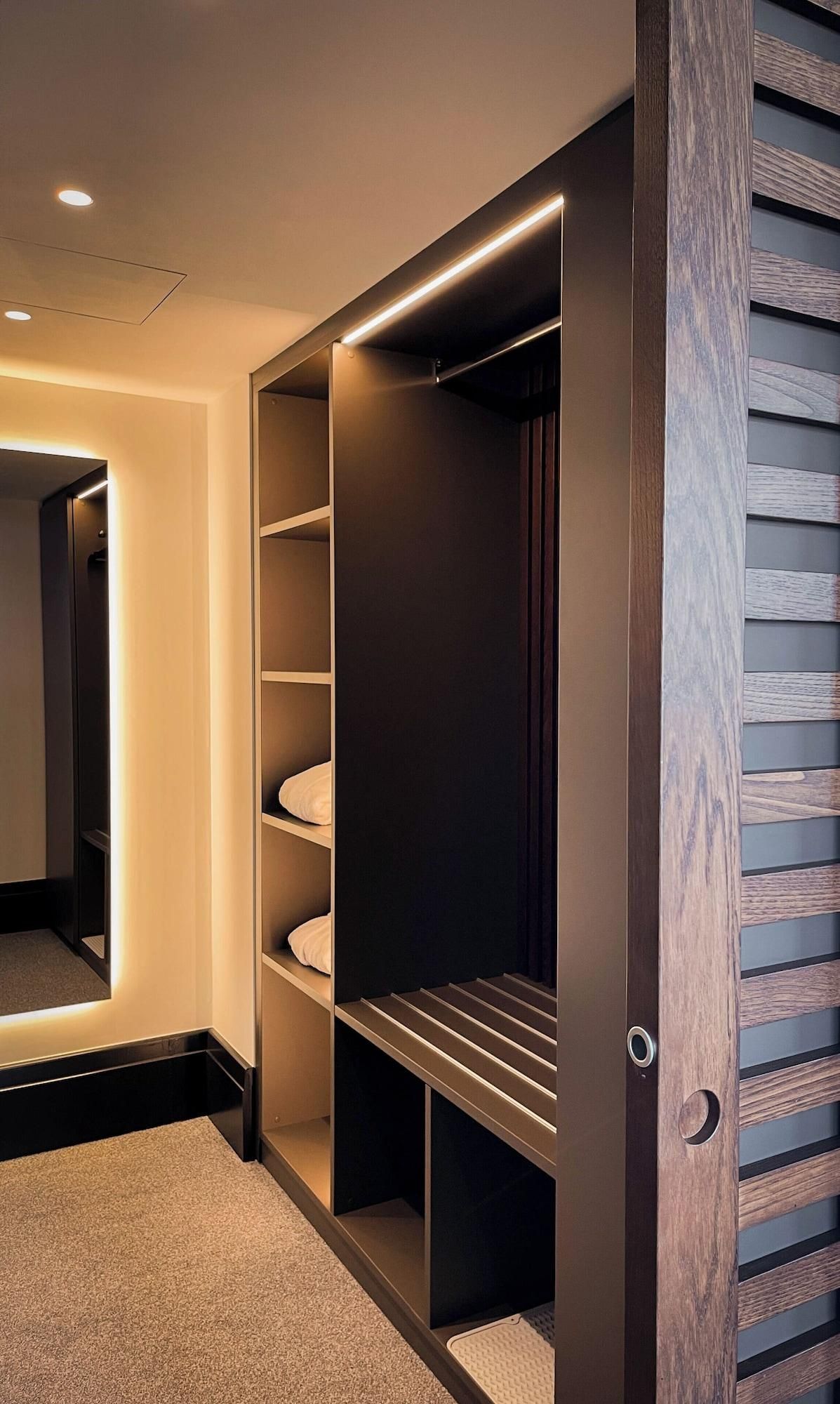 Ein begehbarer Kleiderschrank mit integrierter Beleuchtung, mehreren Ablagen und einer Spiegelklappe.