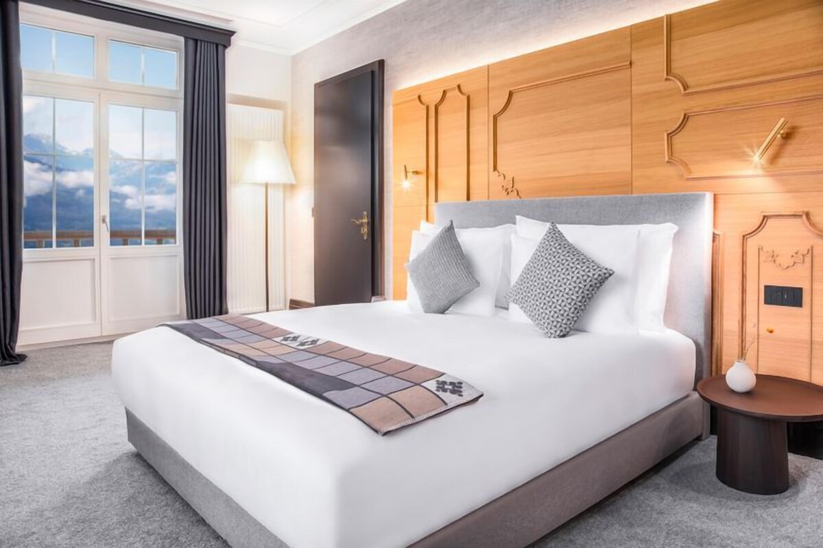 A hotel room with a large bed, wooden headboard, and a view of the mountains through the window.