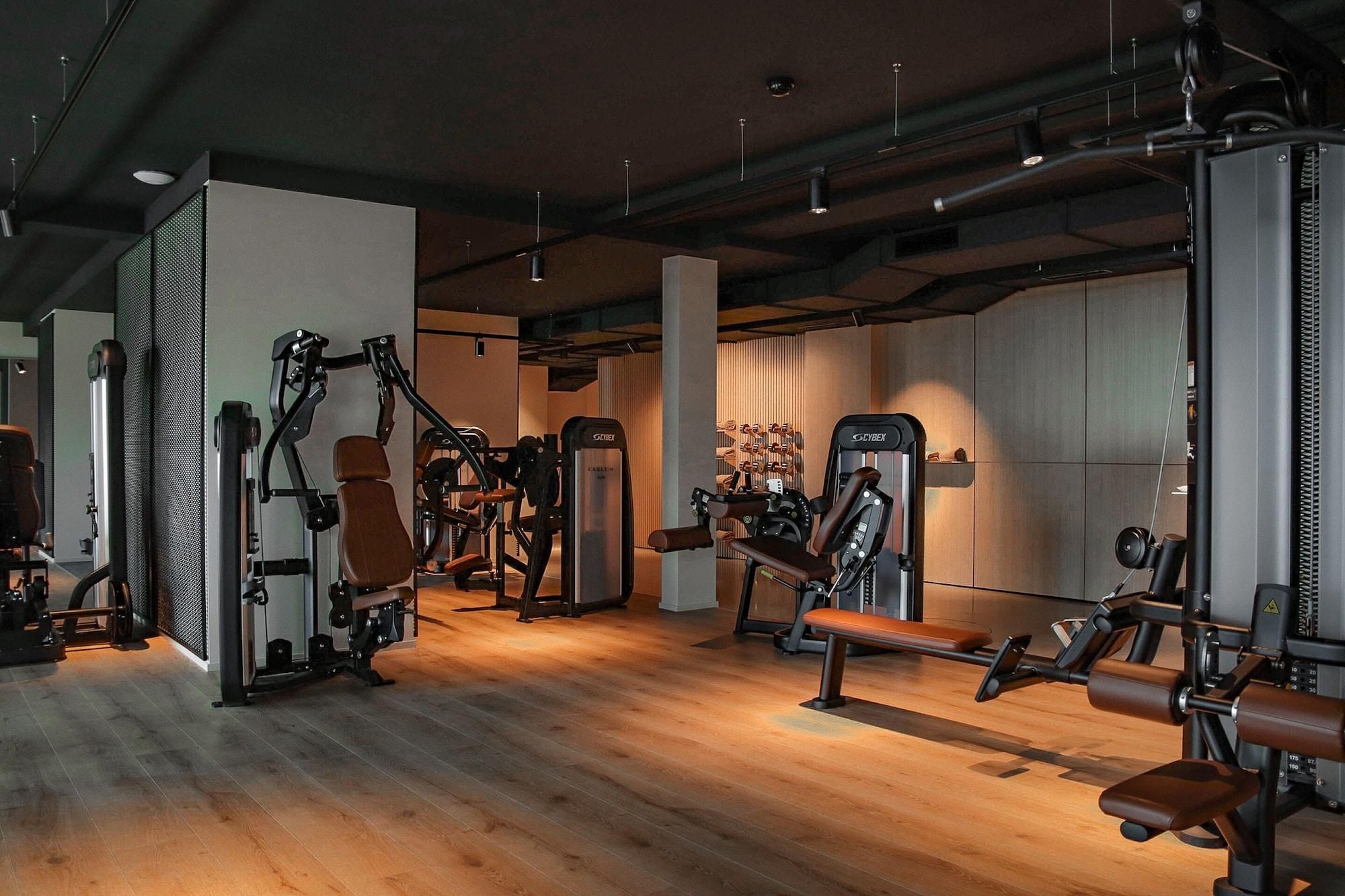 Ein Fitnessstudio mit verschiedenen Trainingsgeräten, Holzboden und modernem Industriedesign.