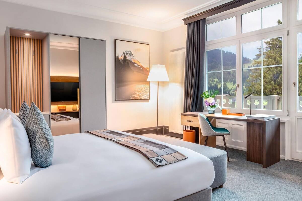A hotel room with a large bed, a desk, a chair, a lamp, and a window with a view of the outdoors.