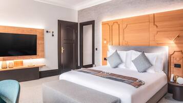 A modern hotel room with a large bed, a TV mounted on the wall, a wooden headboard, and a bedside table with a lamp.