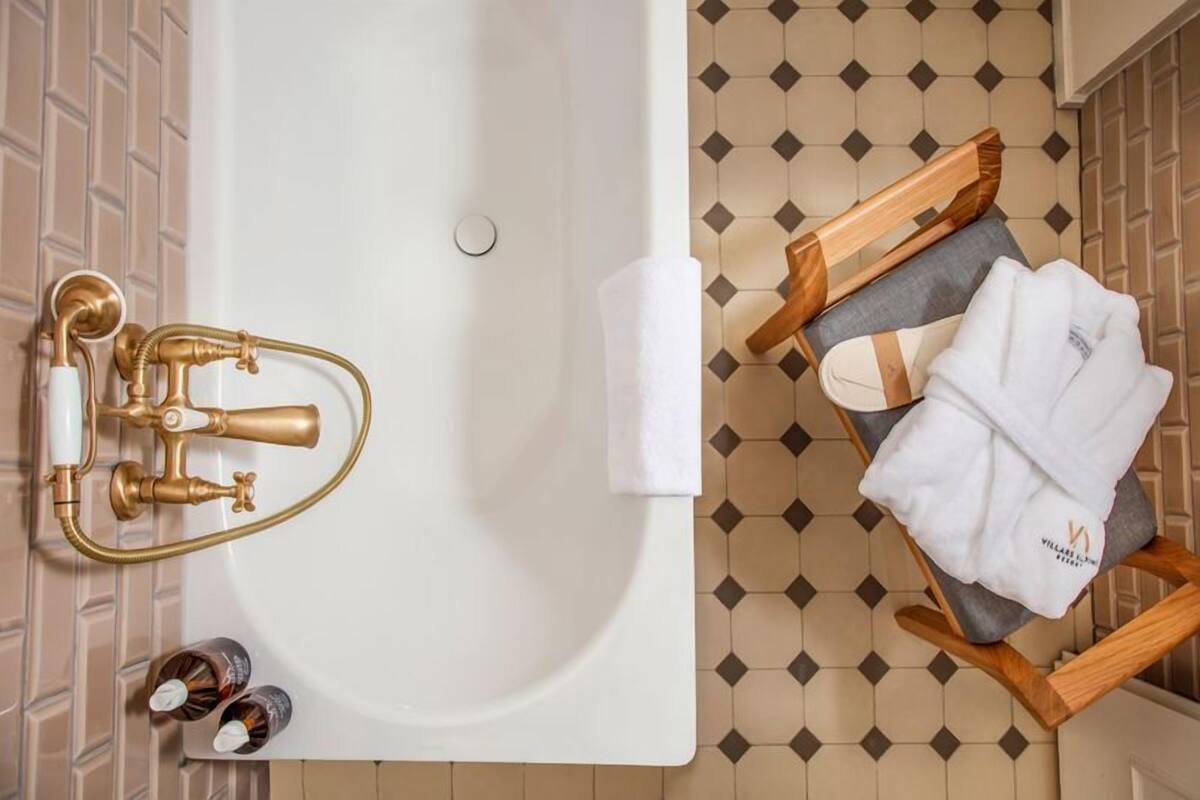 A bathroom with a bathtub, a wooden chair with towels, and a tiled floor.