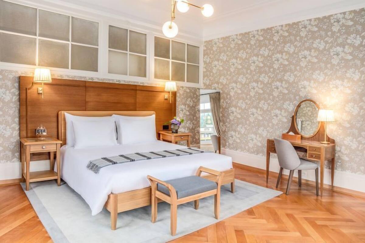 A bedroom with a large bed, wooden headboard, two bedside tables, a desk with a chair, and a large mirror.