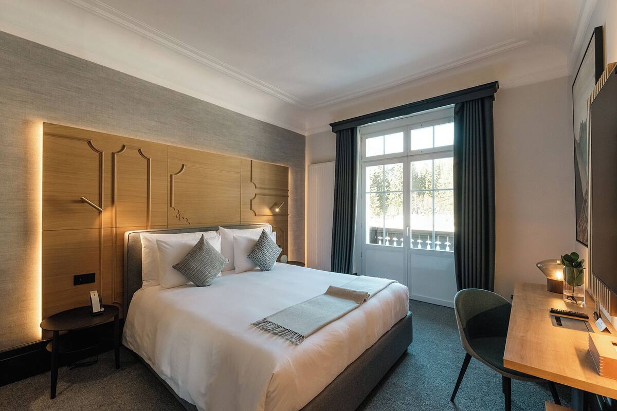 A hotel room with a large bed, a desk, and a window with curtains.