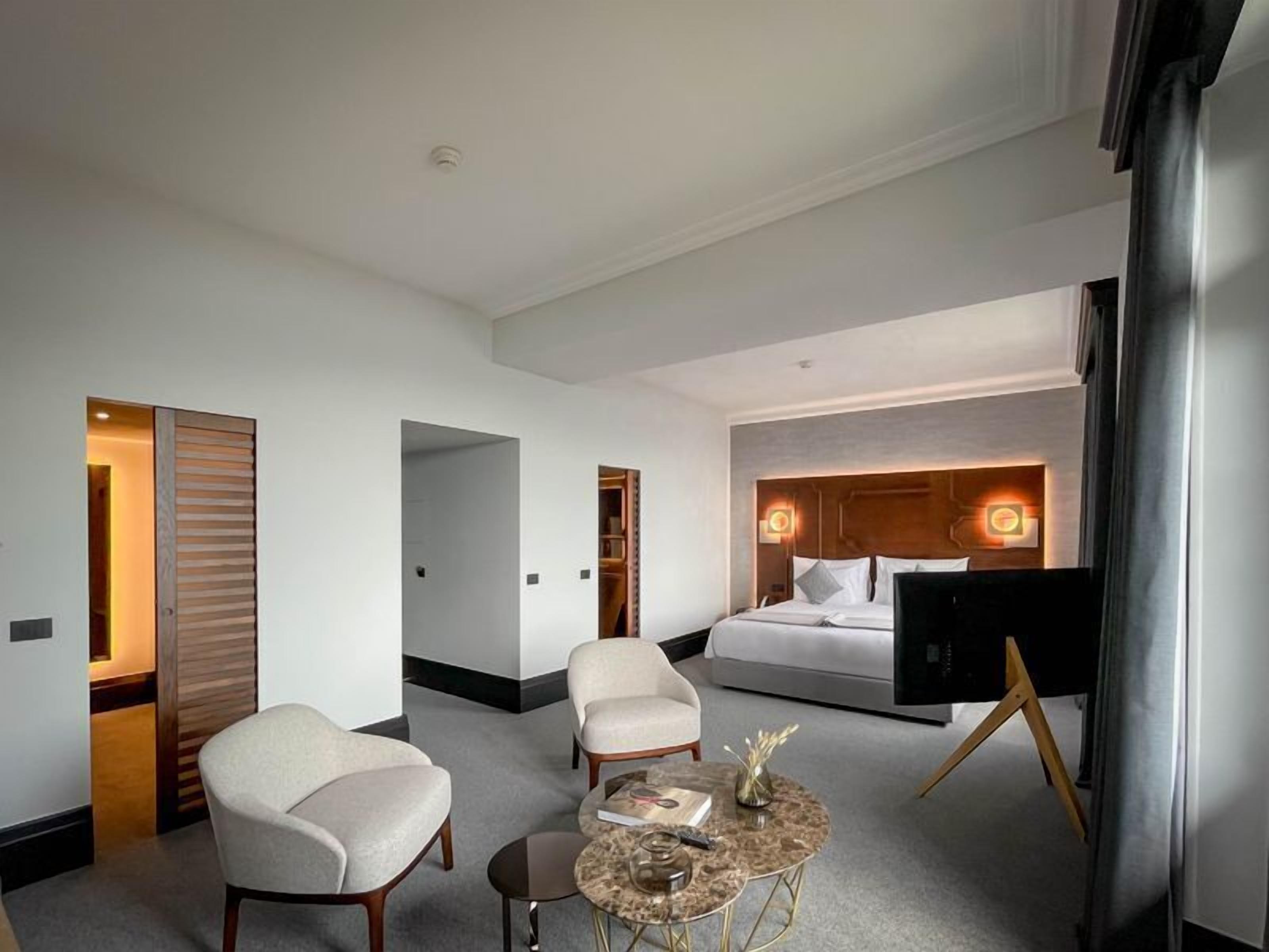 A hotel room with a bed, two armchairs, a small coffee table, and a TV.