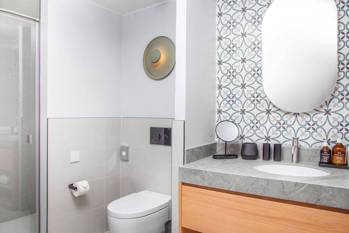 A modern bathroom with a toilet, a sink with a marble countertop, a mirror, and a patterned wall.