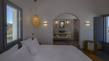 Un dormitorio con una cama grande, una ventana y vistas a un baño con lavamanos y espejo.