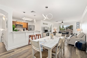 Una cocina moderna con armarios blancos, una isla central y un comedor con una mesa y sillas blancas.