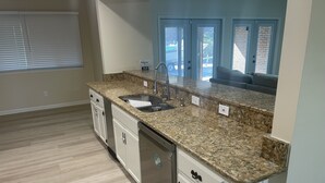Una cocina con encimera de granito, pileta de acero inoxidable y muebles de cocina blancos.