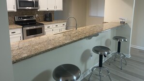 Una cocina moderna con armarios blancos, electrodomésticos de acero inoxidable, encimera de granito y una zona con taburetes de bar.