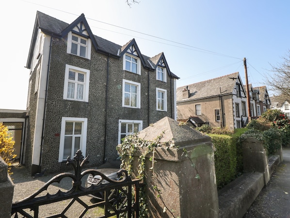 A two-story stone house with a traditional design, featuring a stone facade, white window frames, and a pitched roof.