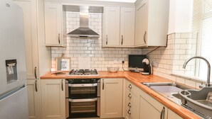 Una cocina compacta con horno integrado, estufa a gas, pileta y ventana con persianas.