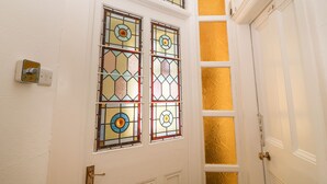 Puerta blanca con pomo de latón y cerradura, junto a una pared con cuatro vidrieras con diseños geométricos.