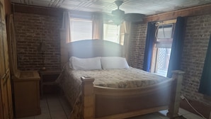Een slaapkamer met een houten bed, een nachtkastje, een bakstenen muur en een raam met jaloezieën.