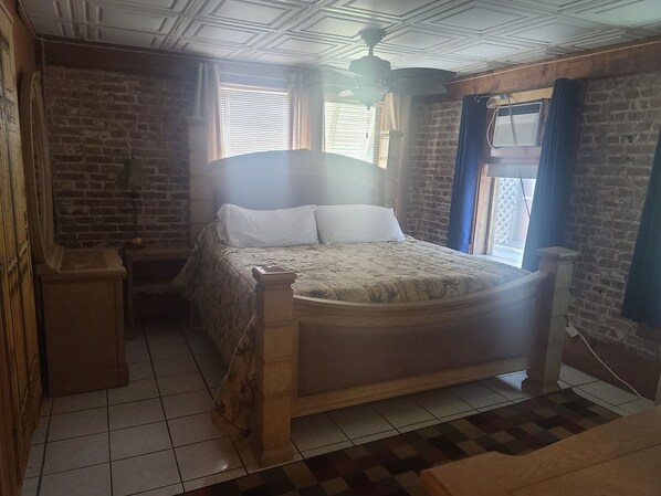 Een slaapkamer met een houten bed, een nachtkastje, een bakstenen muur en een raam met jaloezieën.